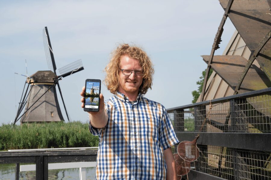 Persoon die telefoon ophoud met daarop onze online gids met daarachter een molen